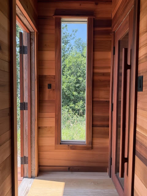 Cedar-lined hallway with a tall narrow window looking out to trees, doors open on either side
